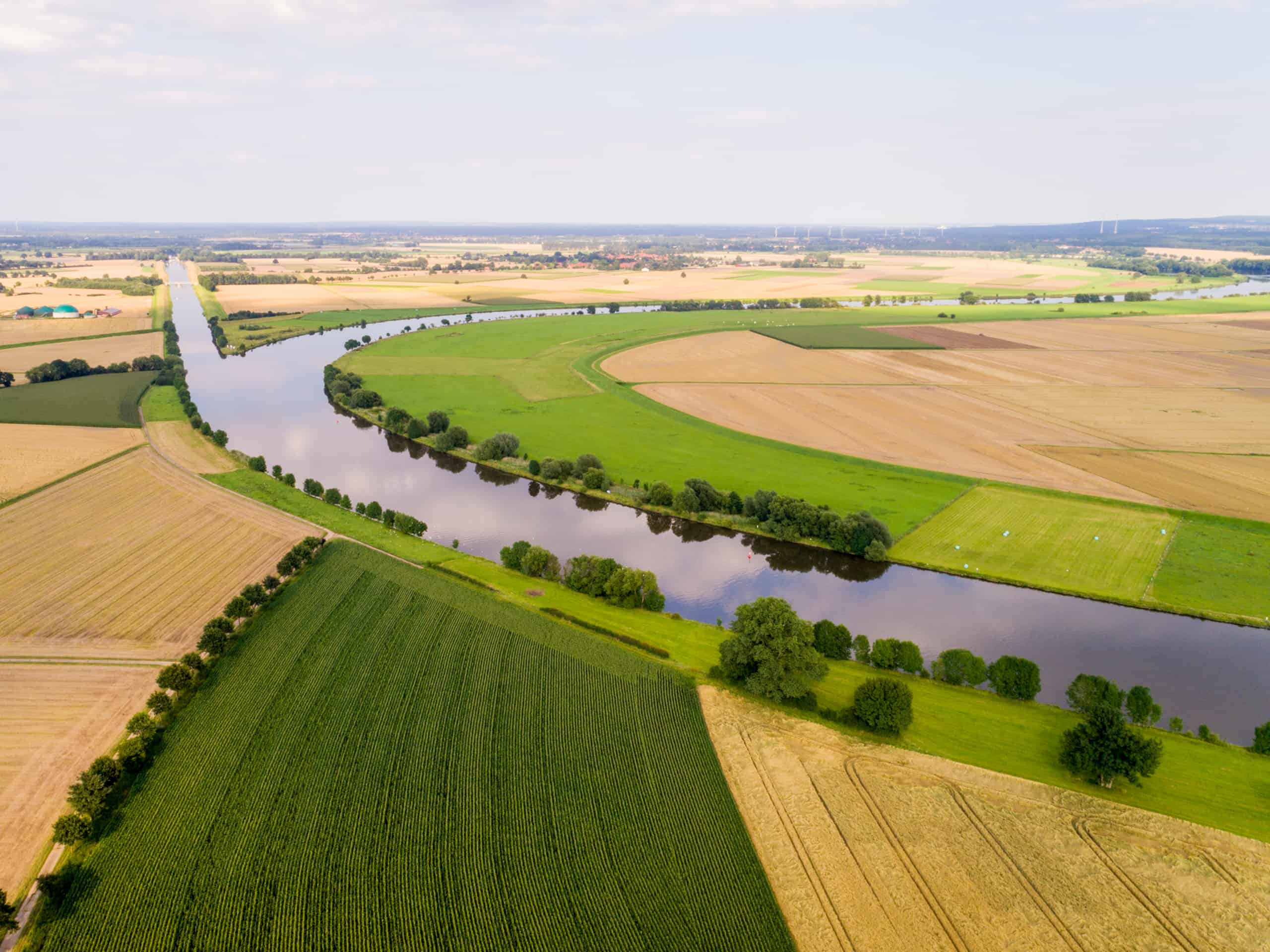 Fluss mit Gewässerrandstreifen fließt durch eine Landwirtschaftlich genutzte Umgebung 