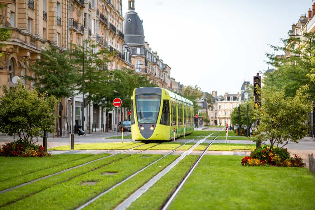 Eine Straßenbahn fährt auf einem Gleis durch eine Stadt. Zwischen den Gleisen ist eine Grünfläche.