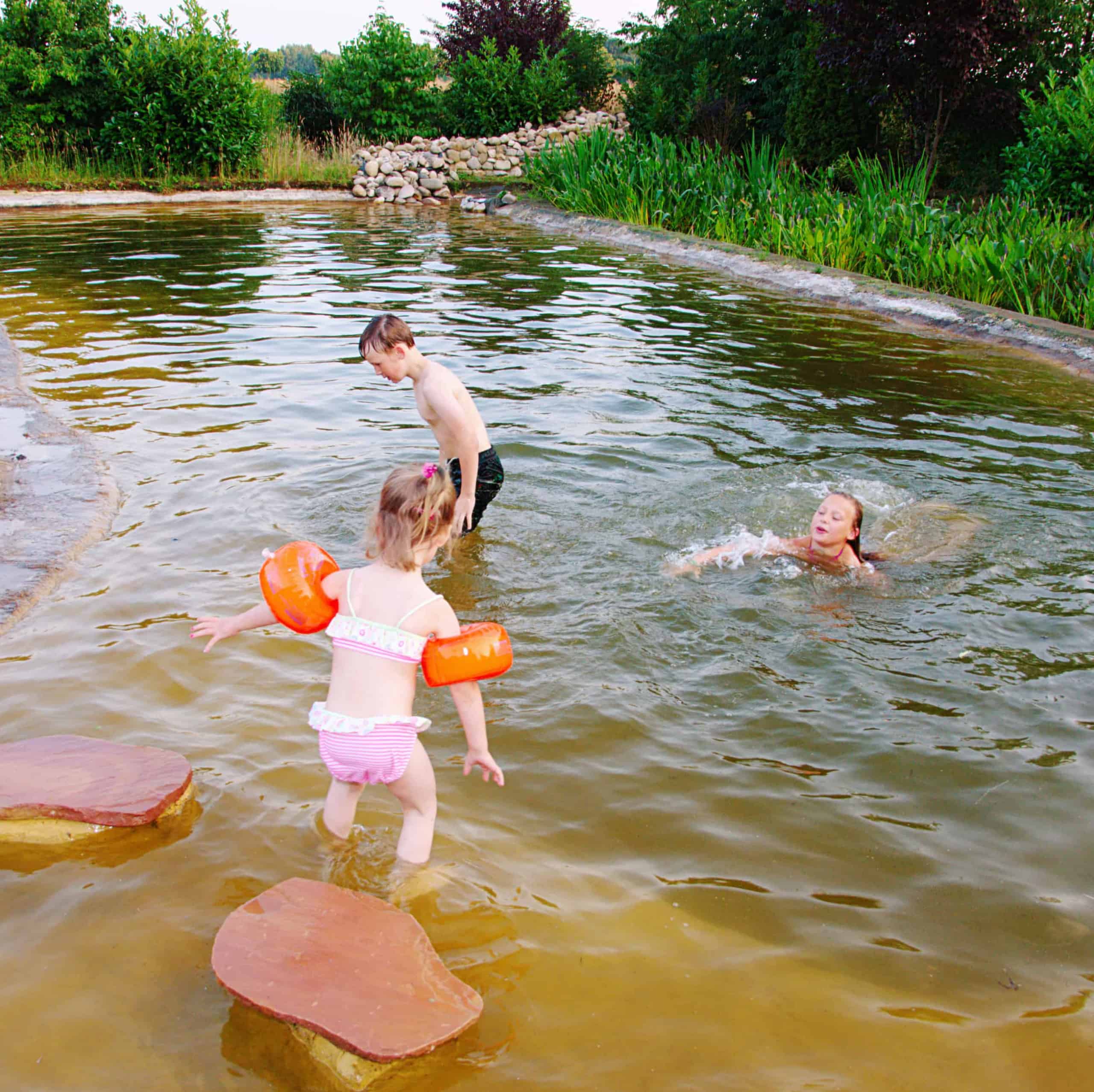 Drei Kinder spielen im Badeteich