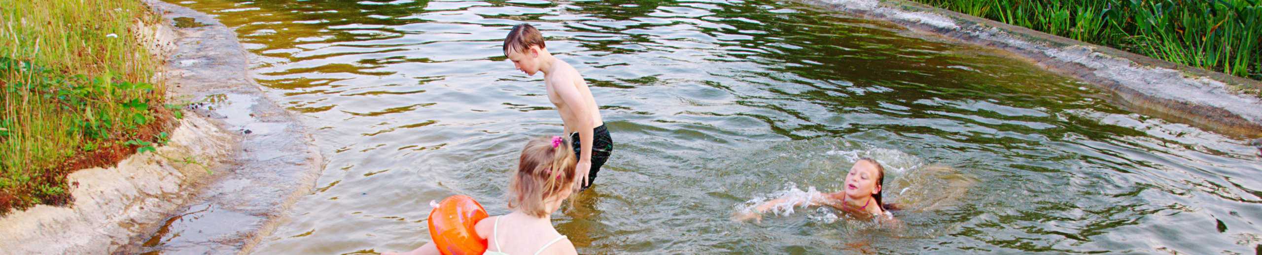 Planschende und schwimmende Kinder in einem Teich