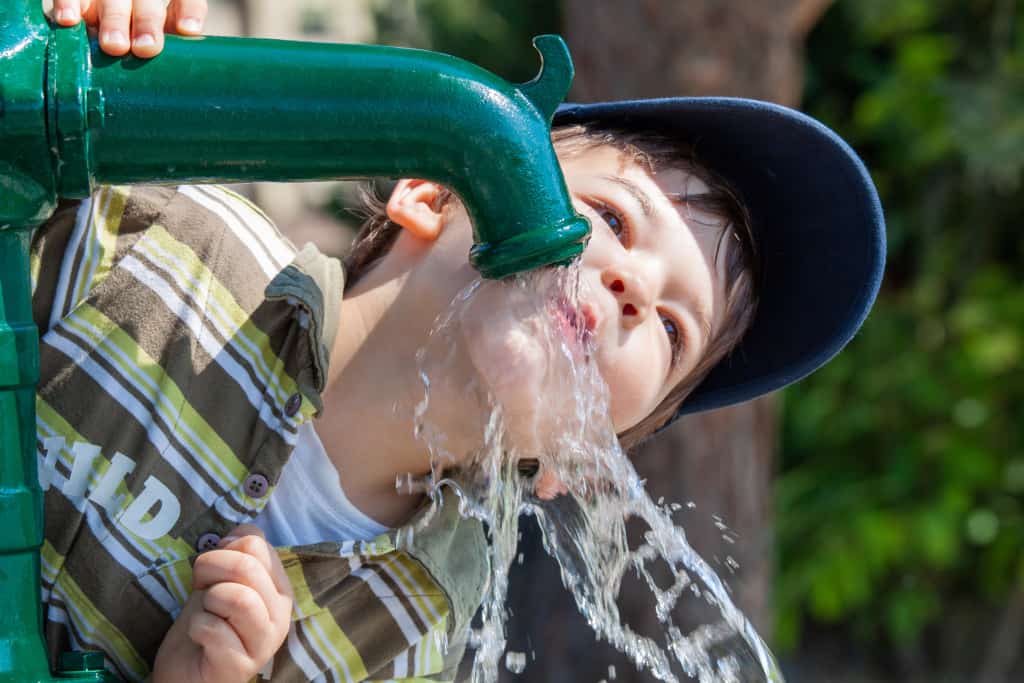 Ein Junge trinkt von einer Pumpe