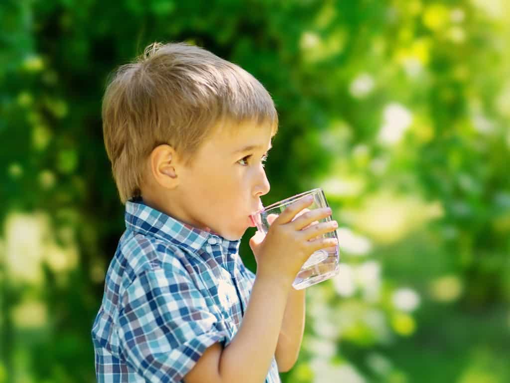 Ein Junge trinkt aus einem Glas. Als Symbol für eine Große Trinkwasseranalyse.