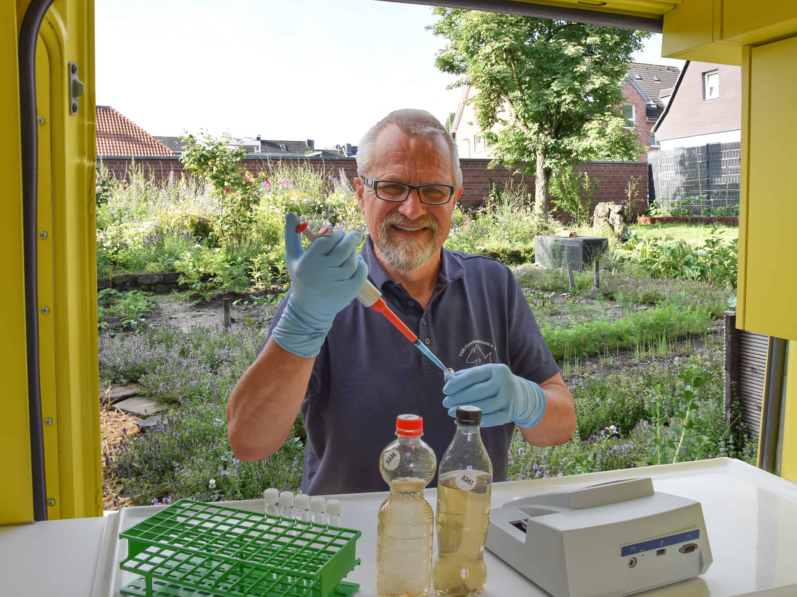 Harald Gülzow analysiert eine Brunnenwasserprobe in einem Garten am Labormobil