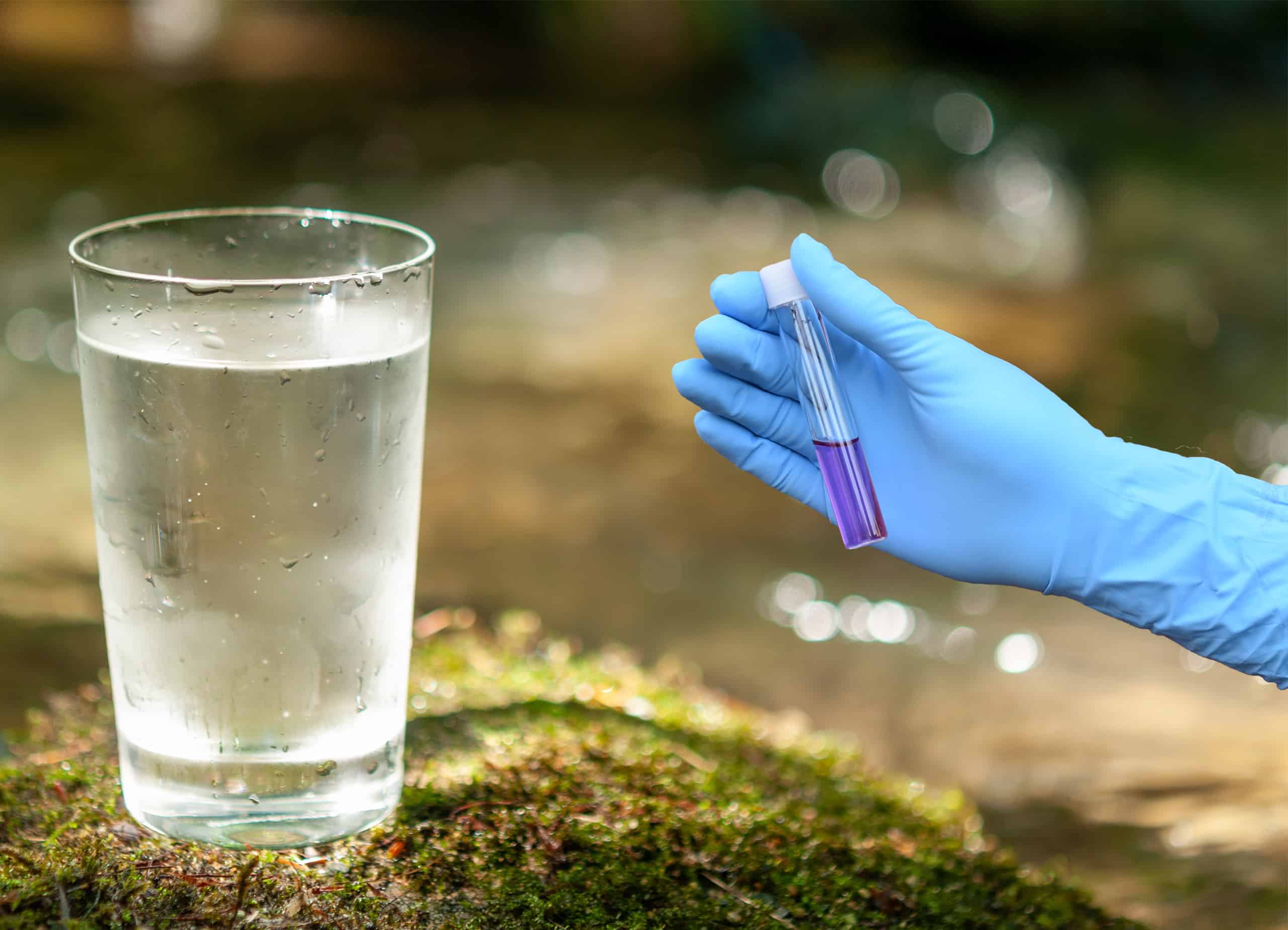 Ein Nitrat-Röhrchen wird neben einem Trinkwasser-Glas gehalten