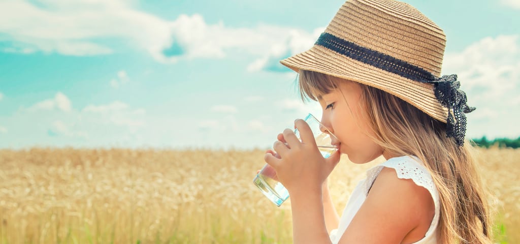 Ein Mädchen trinkt Wasser aus einem Glas in der Nähe eines Weizenfeldes.