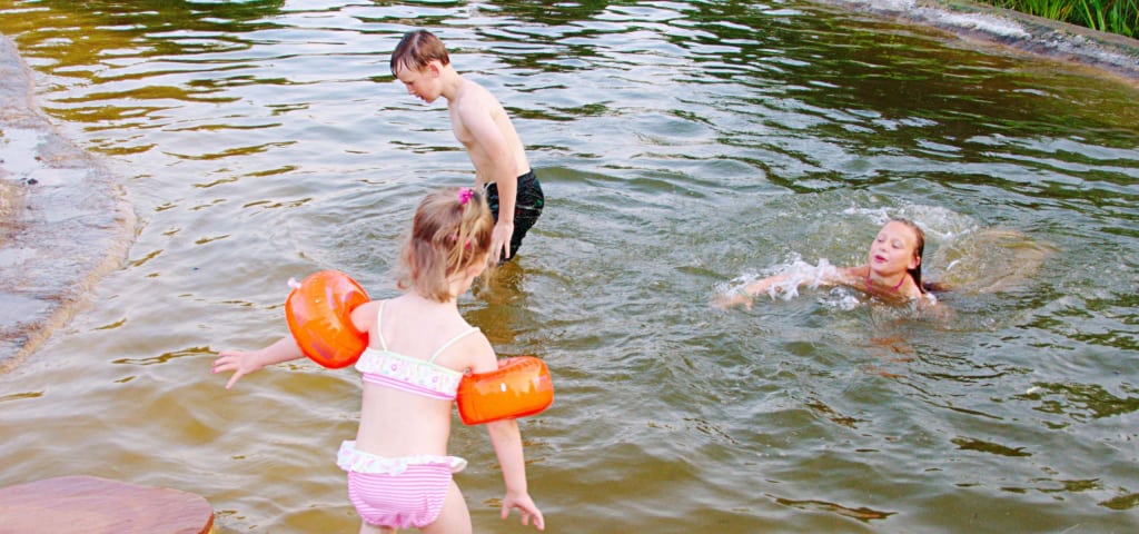 Drei Kinder planschen in einem Teich