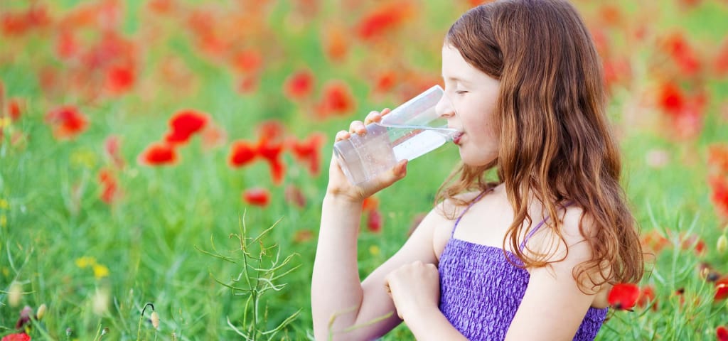Mädchen trinkt Mineralwasser vor einem Mohnfeld