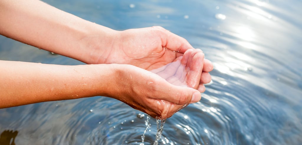 Hände schöpfen Wasser aus einem Gewässer