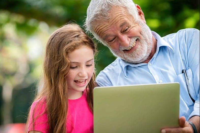 Ein Mann und ein junges Mädchen grinsen und lachen während sie auf ein Tablet schauen.
