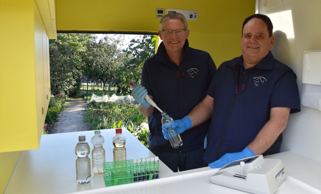 Matthias Ahlbrecht (links) und Ehrenamtler Frank Sombrowski (rechts) untersuchen eine Brunnenwasserprobe im Labormobil vom VSR-Gewässerschutz e.V.