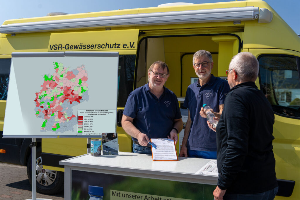 Arno Mittelmeyer und Heinz-Theo van Wickeren beraten einen Brunnenbesitzer mit Nitratkarte Deutschland vor einem Labormobil des VSR-Gewässerschutz e.V. Fotograf Ruben Wiltsch