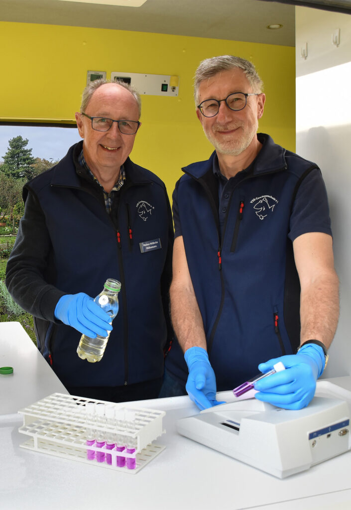 Heinz-Wilhelm Hülsmans (links) und Heinz-Theo van Wickeren (rechts) untersuchen eine Brunnenwasserprobe im Labormobil vom VSR-Gewässerschutz